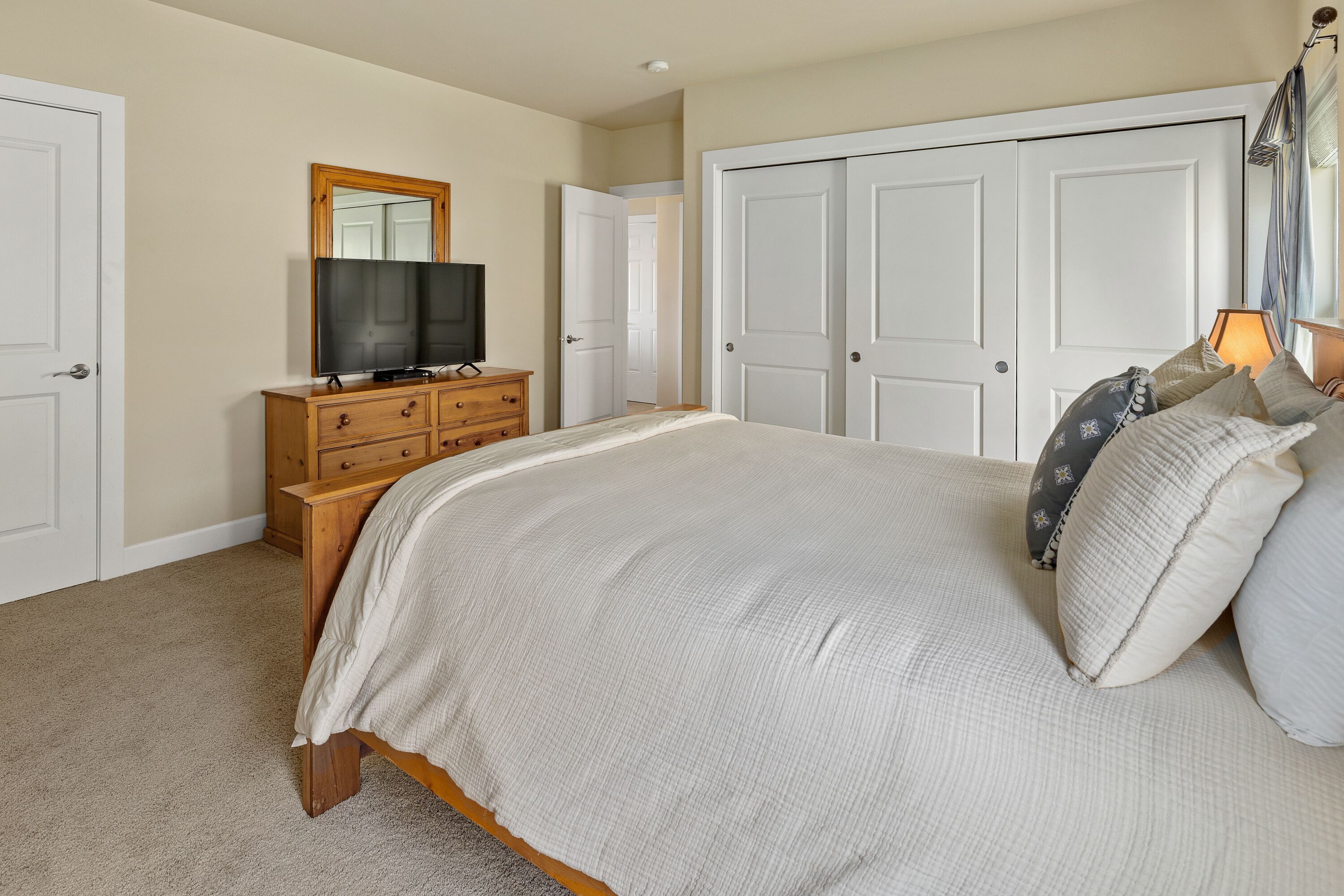 A bedroom with a large bed, a dresser, a television, and a wardrobe.