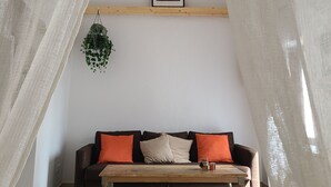 A cozy room with a wooden bench, a cushioned sofa with orange cushions, a hanging plant, and a framed picture on the wall. - 113 Livingtarifa Amapola (Tarifa)