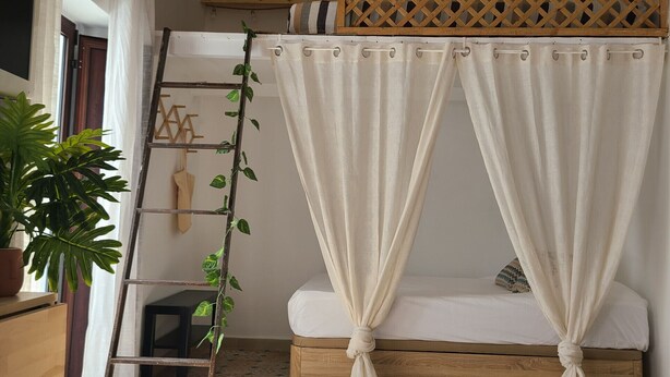 A room with a sloped ceiling, a wooden ladder, a bed with white bedding, and a potted plant. - 113 Livingtarifa Amapola (Tarifa)