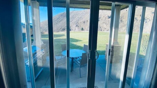 A sliding glass door leading to an outdoor patio with a table and chairs, a grassy lawn, and a mountain in the background.