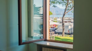 Vista desde una ventana a un puerto deportivo con barcos, tiendas de campaña y una zona verde.