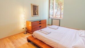 Un dormitorio con una cama de madera, un aparador, un radiador y una ventana con vistas a árboles.