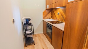 Cocina compacta con horno empotrado, cafetera sobre carrito y armarios de madera.