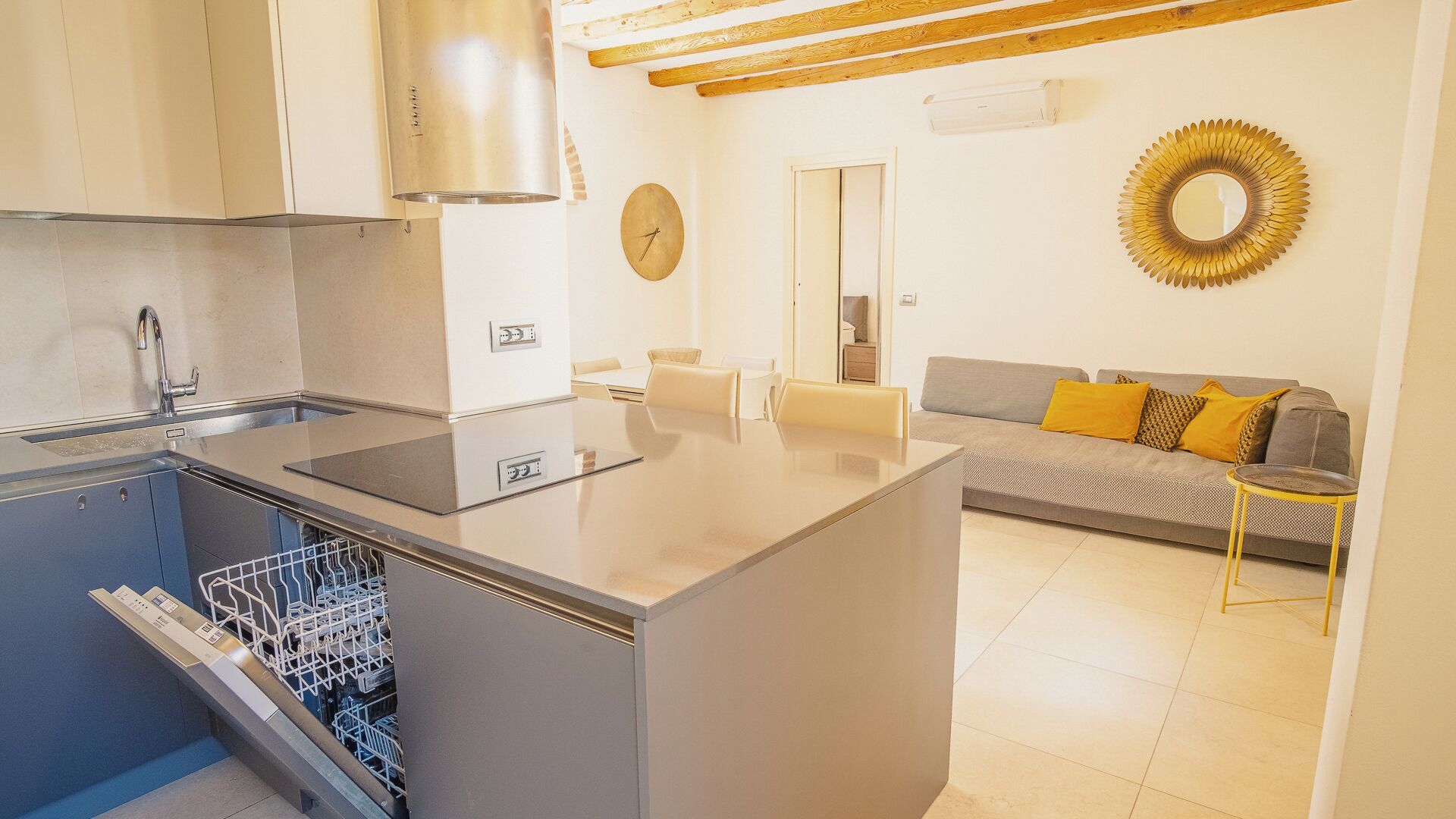 Cocina compacta con lavavajillas, estufa integrada y comedor con sofá y espejo.