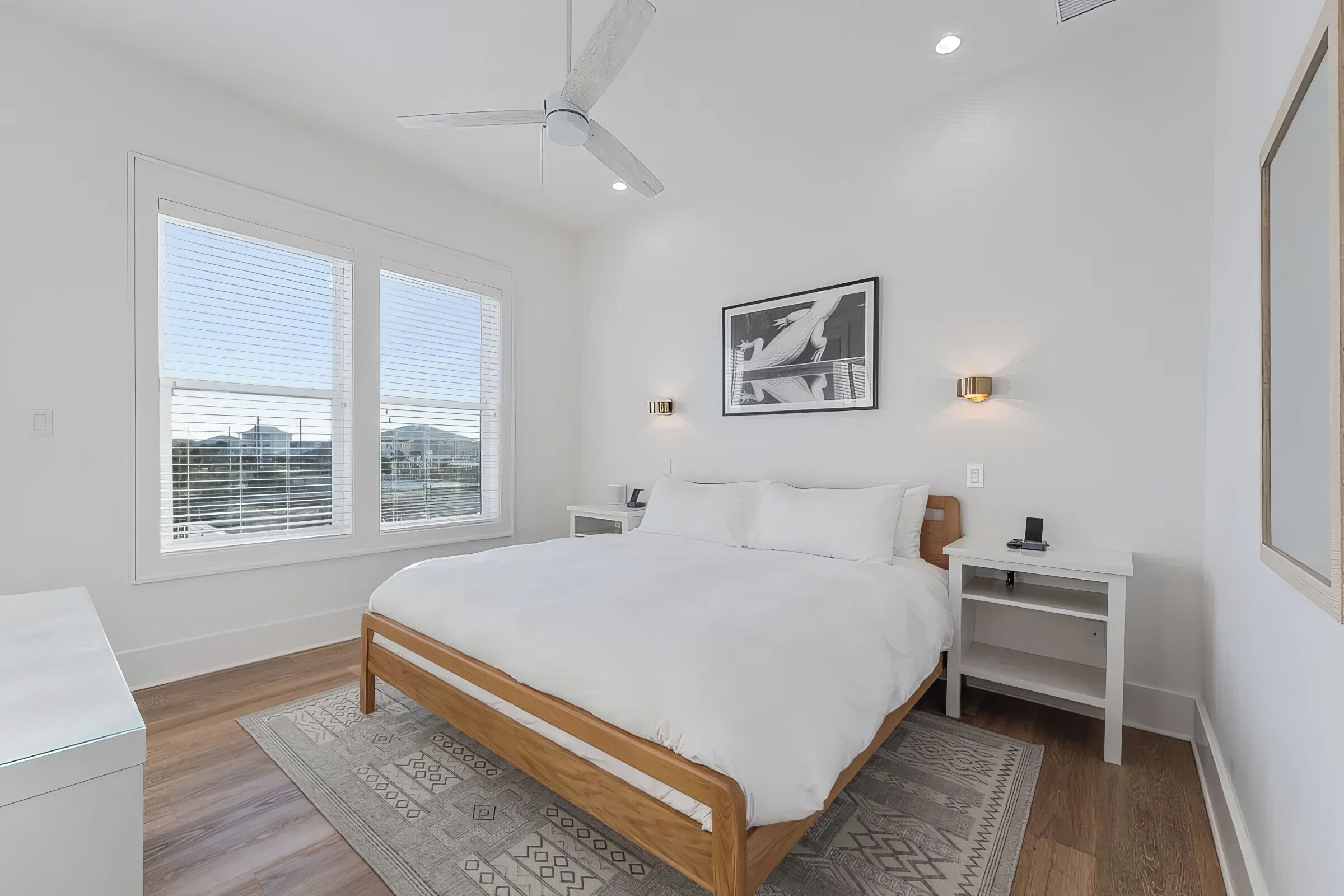 A bedroom with a bed, nightstands, a ceiling fan, a window with blinds, and a framed picture on the wall.