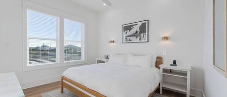 A bedroom with a bed, nightstands, a ceiling fan, a window with blinds, and a framed picture on the wall.