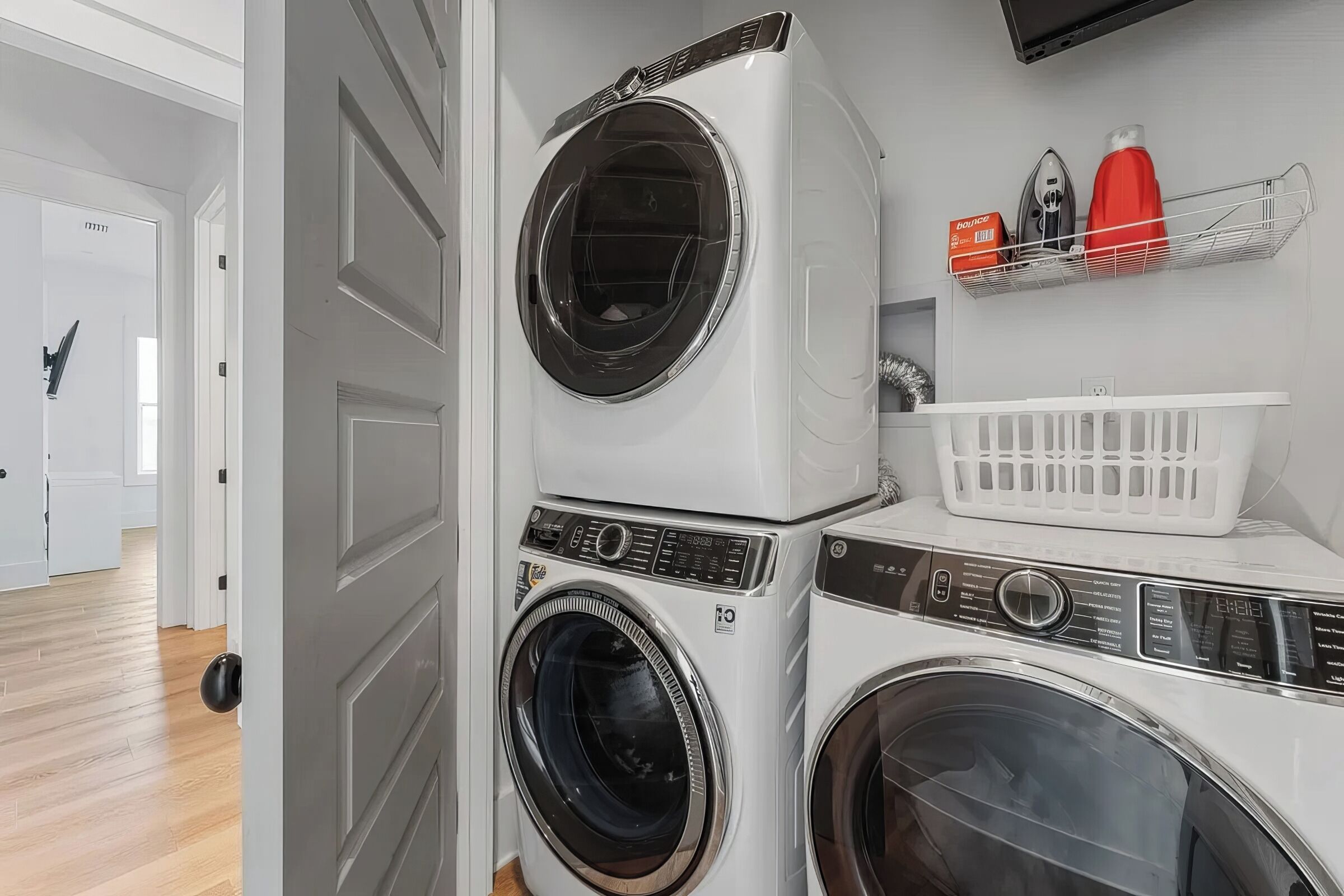 A laundry area with stacked washers and dryers, a shelf with laundry supplies, and a basket.