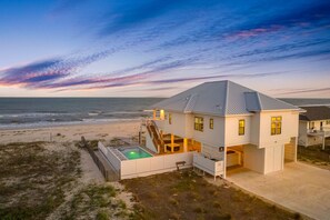 Una casa frente a la playa con piscina, una escalera que sube al nivel superior y vista al océano.