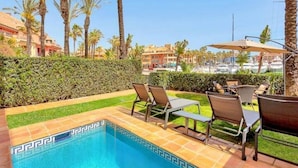 Una piscina con lettini e ombrelloni, circondata da palme e vista su un porto turistico.