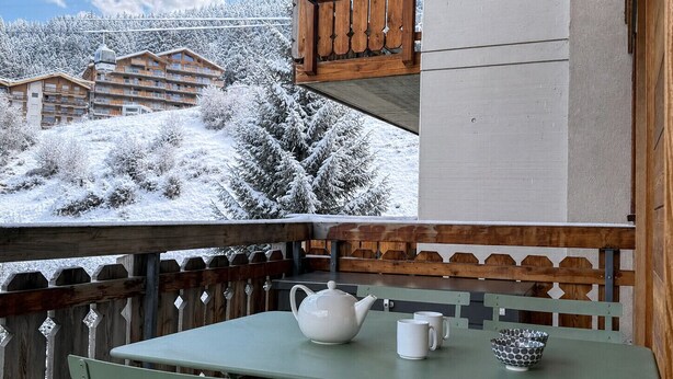 A balcony with a table and chairs, a wooden fence, and a view of snow-covered buildings and trees. - Pracondu 2 203 - OUTDOOR & FUN apartment 5 pers (Haute-Nendaz)