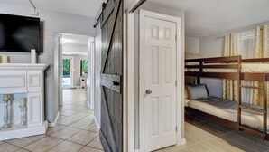 Una habitación con literas, una puerta blanca y un televisor sobre un mueble.