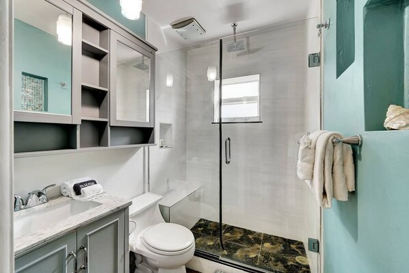 A modern bathroom with a glass-enclosed shower, a white toilet, and a vanity with a mirror and shelves.
