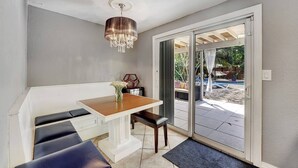 Un pequeño comedor con mesa y bancos, una araña y una puerta corrediza de vidrio que da a un patio exterior con piscina.