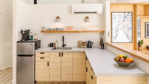 Une cuisine moderne dotée d’un réfrigérateur encastré, de meubles en bois, d’un évier en acier inoxydable et d’un panier à fruits posé sur le plan de travail.