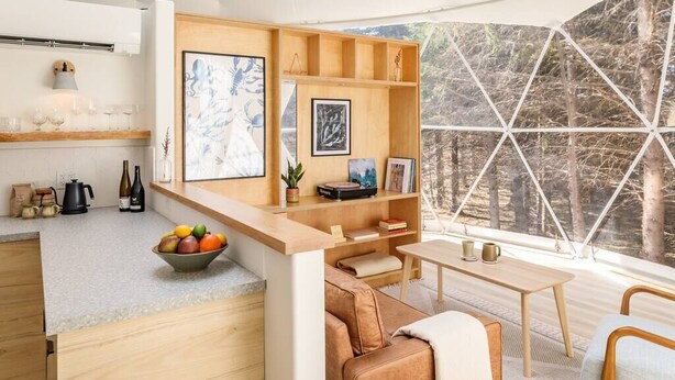 Une cuisine moderne avec un plan de travail en bois, un saladier rempli de fruits et un coin repas comprenant une table et des chaises.