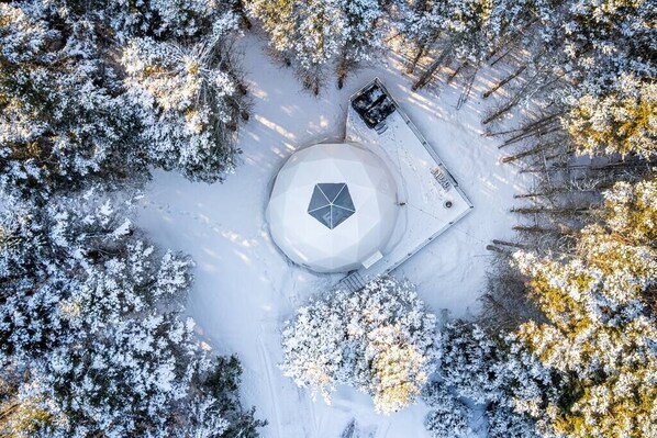 An aerial view of a snow-covered area with a circular structure, possibly a gazebo or pavilion, surrounded by trees. - Maytree Eco-Retreat, Maytree Eco-Retreat | PEI (Prince Edward Island)