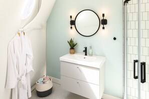 A bathroom with a white vanity, a round mirror, a potted plant, and a glass shower enclosure. - Maytree Eco-Retreat, Maytree Eco-Retreat | PEI (Prince Edward Island)