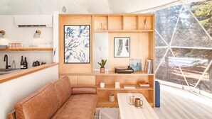 Un intérieur moderne avec un canapé en cuir marron, des étagères en bois et une grande fenêtre donnant sur la forêt.