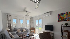 A modern living room with a ceiling fan, large windows, a sofa, a coffee table, and a TV.