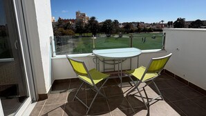 A balcony with a table and chairs, a view of a park, and a distant building.