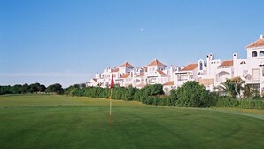 A golf course with a red flag on the green, surrounded by white buildings with red-tiled roofs.