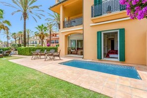 A hotel with a swimming pool, outdoor seating, and a balcony with green shutters.