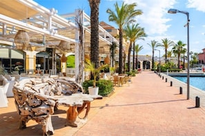A waterfront hotel with outdoor seating, palm trees, and a pool.