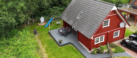 A red house with a sloped roof, a patio with outdoor furniture, and a swing set.