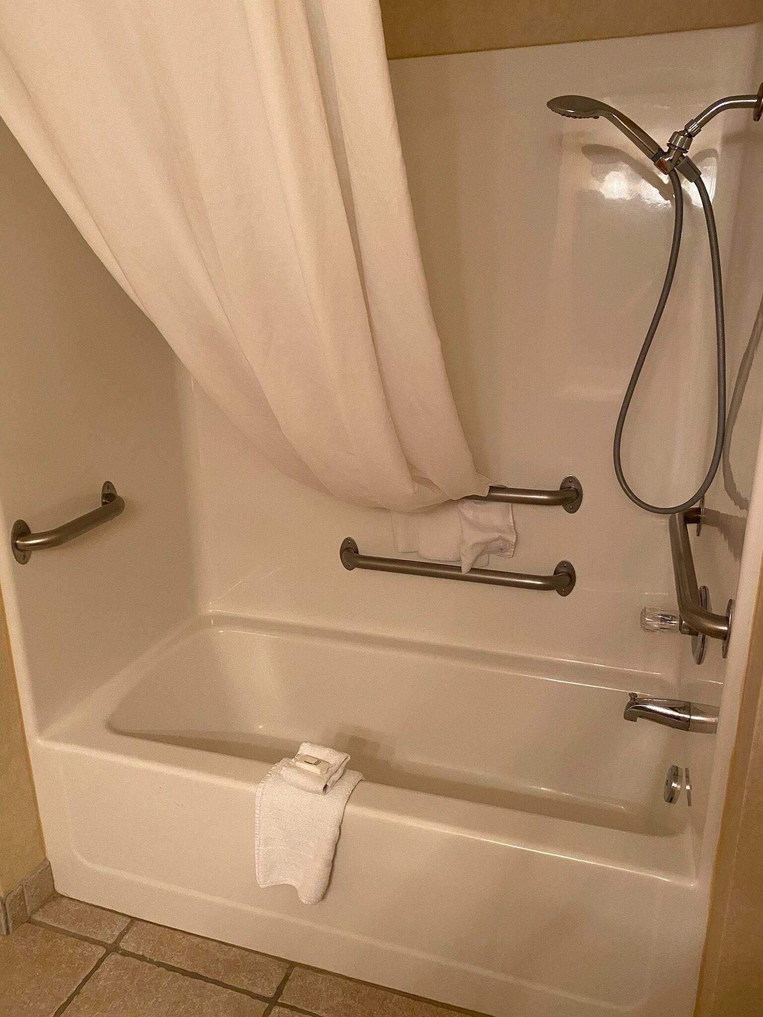 A standard bathtub with a shower head, grab bars, and a towel rack.