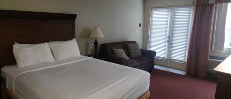 A hotel room with a large bed, a chair, a lamp, and a window with blinds.