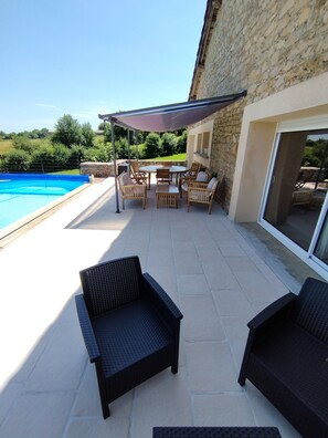 A patio with a pool, outdoor furniture, and a stone building.