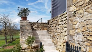 Una escalera de piedra conduce a un edificio con una verja de metal, rodeado de follaje y un cielo despejado.