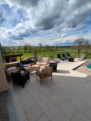 An outdoor patio area with seating arrangements, a barbecue grill, and a view of the countryside.