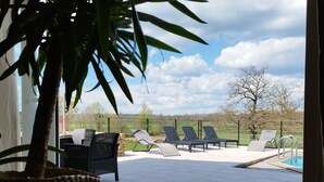 Un patio con sillones de descanso, una piscina y vistas al campo.
