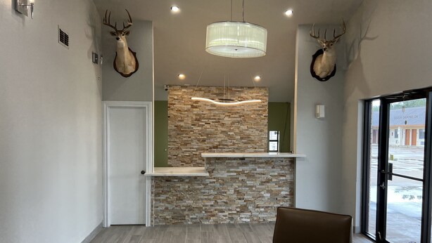 A reception area with a stone wall, a wooden reception desk, a brown leather chair, and two mounted deer heads.