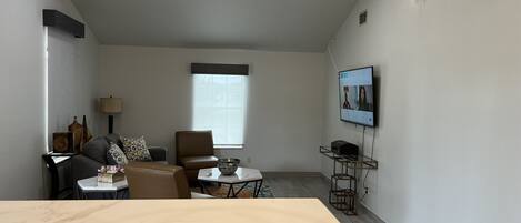 A modern living room with a marble coffee table, a sofa, a TV mounted on the wall, and a window with blinds.