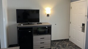 A compact hotel room with a flat-screen TV, a small refrigerator, a microwave, and a minibar.