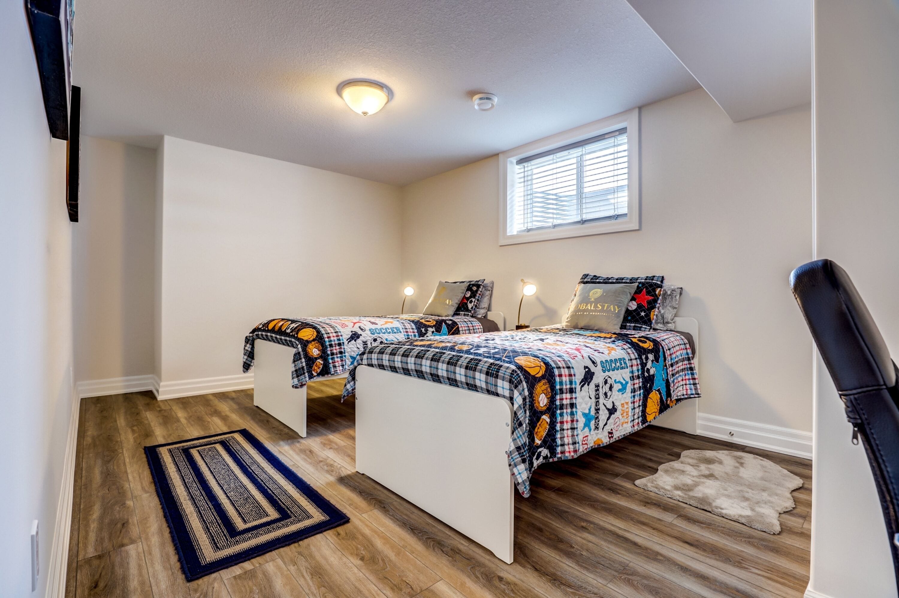 A bedroom with two beds, a window, a ceiling light, and a rug.