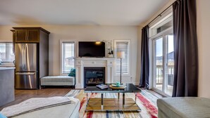 A modern living room with a fireplace, a flat-screen TV, a dining table, and a kitchen area with a refrigerator. - GLOBALSTAY Brand New House in Port Elgin (Saugeen Shores)