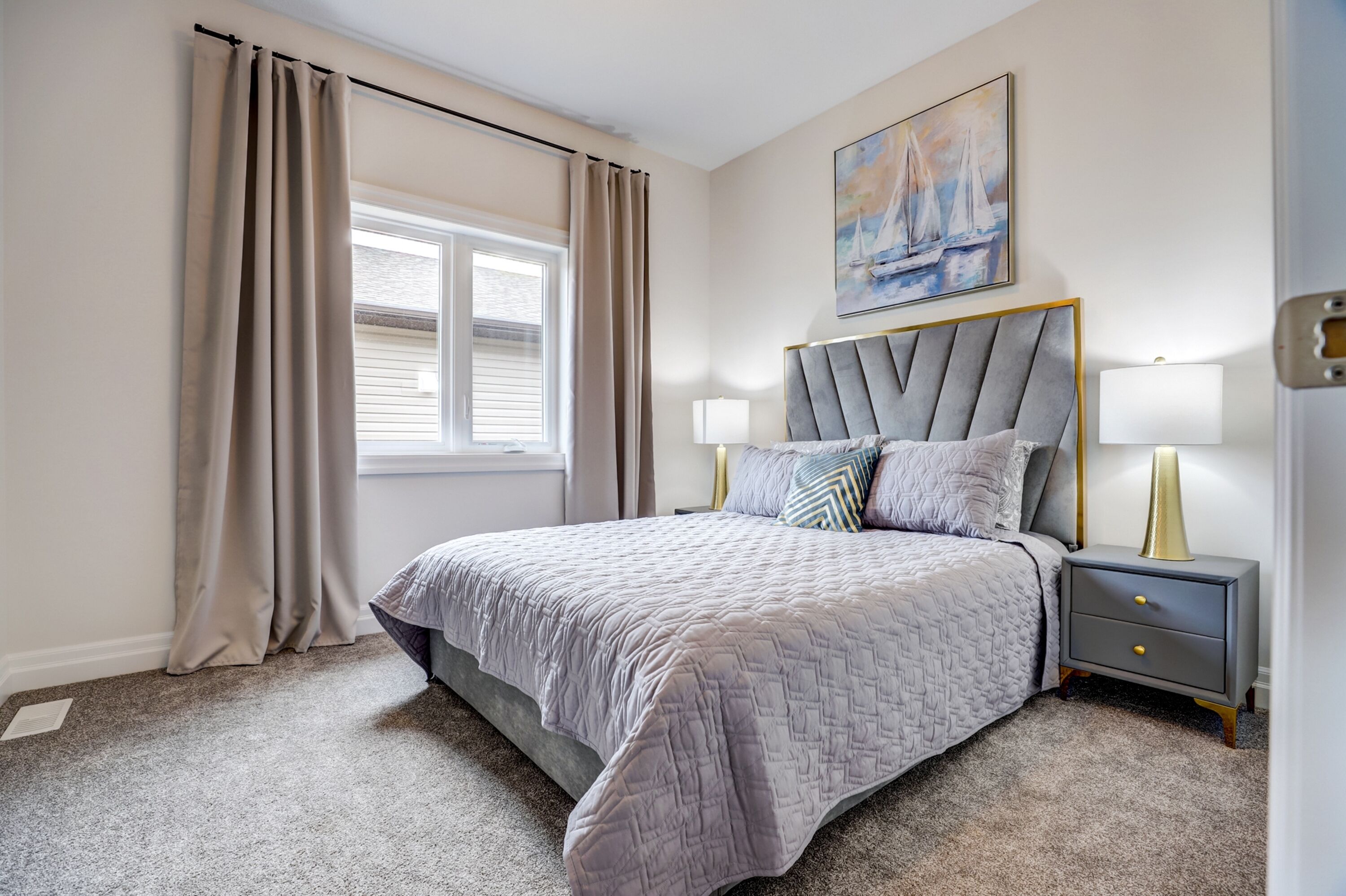 A bedroom with a bed, two bedside tables with lamps, a window with curtains, and a painting on the wall.