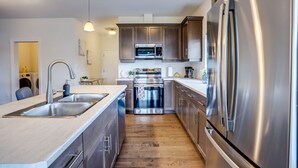 A modern kitchen with stainless steel appliances, wooden cabinets, and a central island with a sink. - GLOBALSTAY Brand New House in Port Elgin (Saugeen Shores)