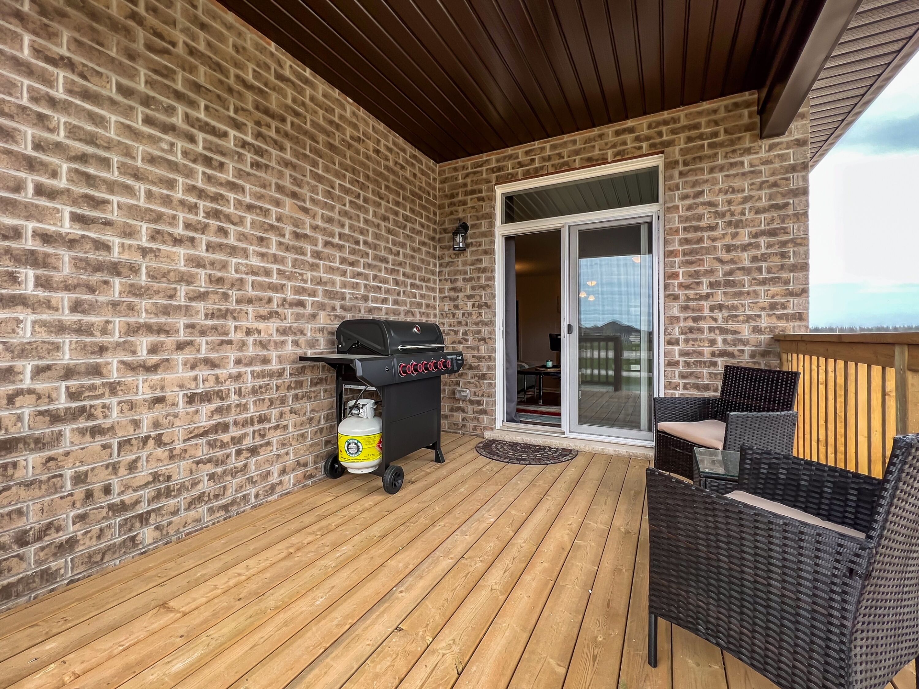 Eine überdachte Terrasse mit Backsteinmauer, Grill, Gasflasche und Korbmöbeln.