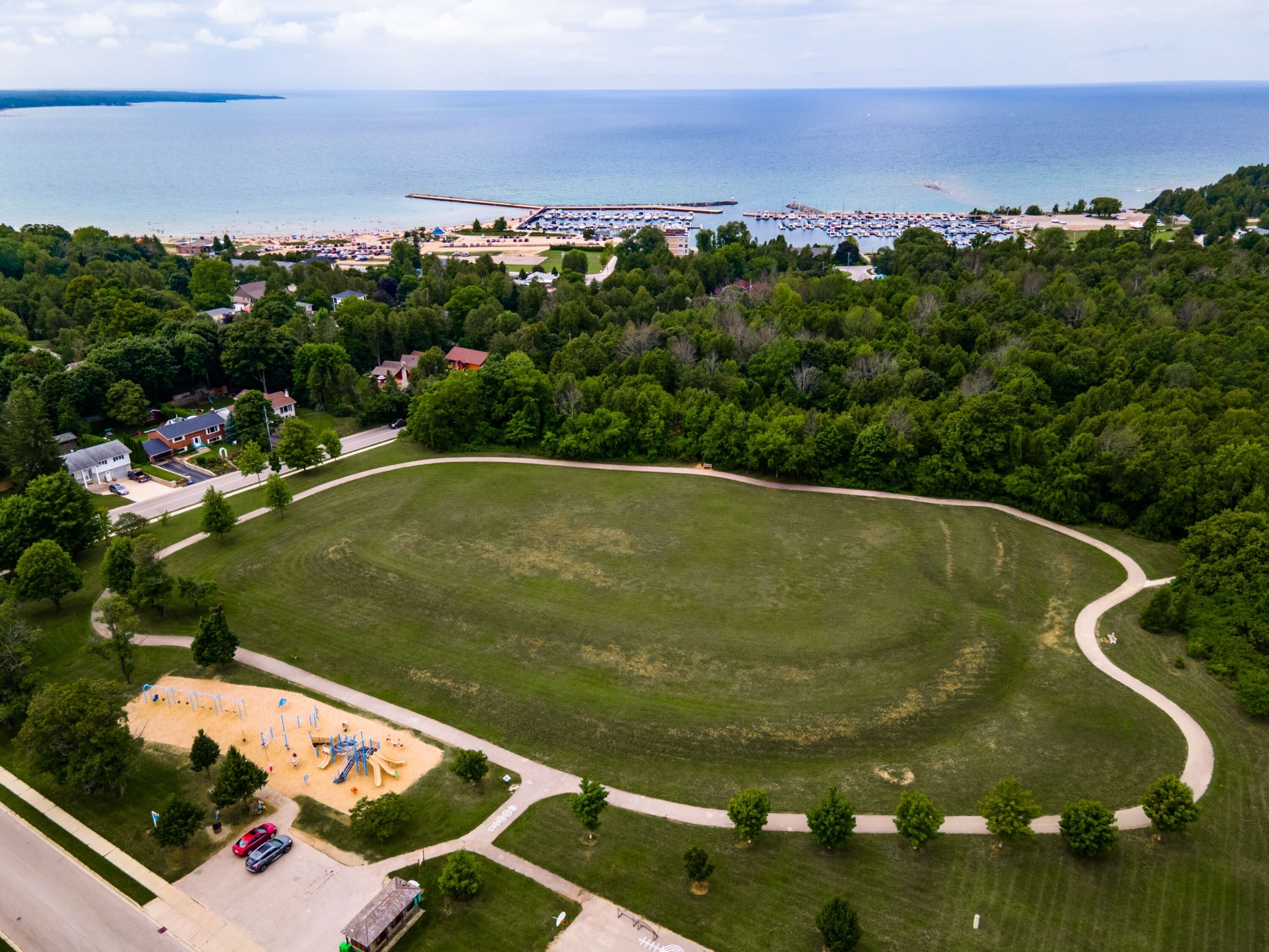 An aerial view of a park with a playground, a road, and a beach area with a pier.