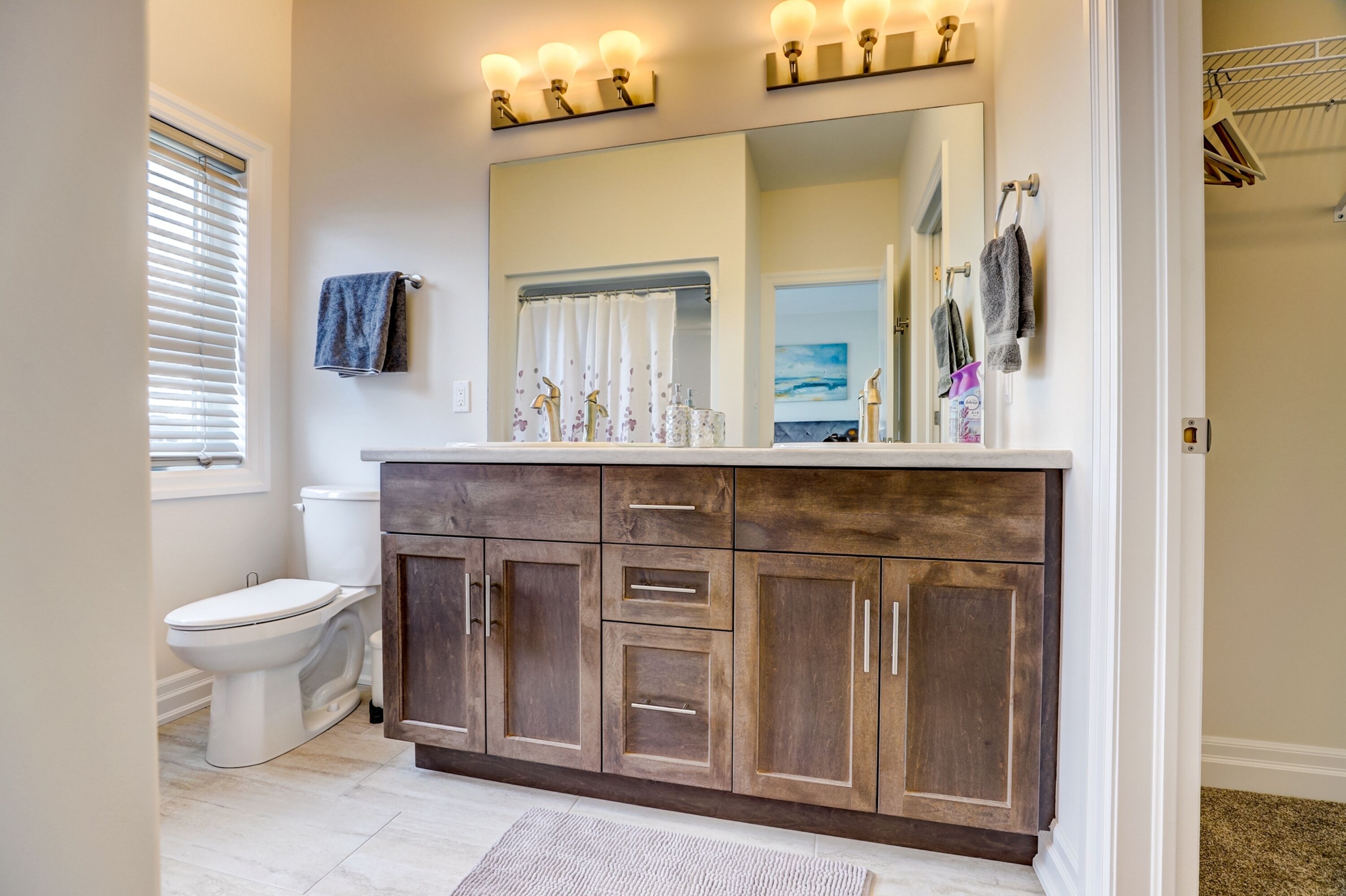 A bathroom with a white toilet, dark wooden vanity, and a large mirror with light fixtures above.