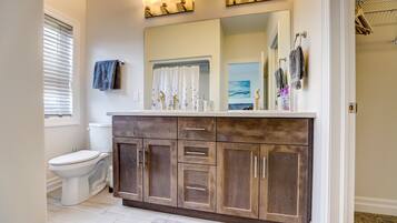 A bathroom with a white toilet, dark wooden vanity, and a large mirror with light fixtures above.