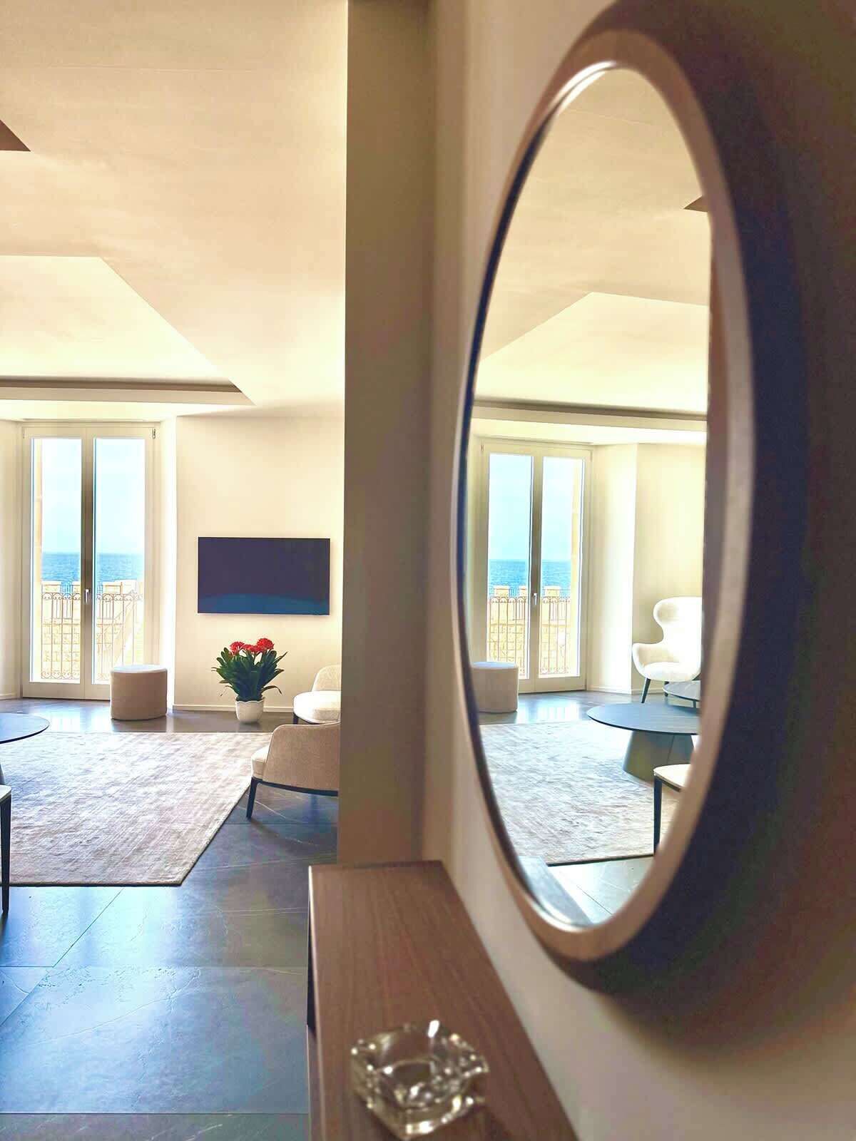 A spacious living room with a large mirror, a flat-screen TV, and a view of the sea through the sliding glass doors.
