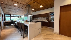 A modern kitchen with a large island, bar stools, and a view of the outdoors. - Vossa Bossa Maresias (São Sebastião)