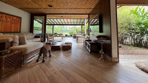 A spacious living area with a wooden floor, a sofa, a coffee table, and a television. - Vossa Bossa Maresias (São Sebastião)