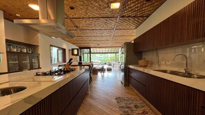 A modern kitchen with a central island, wooden flooring, and a view to a patio area. - Vossa Bossa Maresias (São Sebastião)