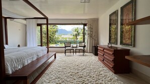 A bedroom with a large bed, a wooden bench, a desk, and a view of a pool and mountains. - Vossa Bossa Maresias (São Sebastião)